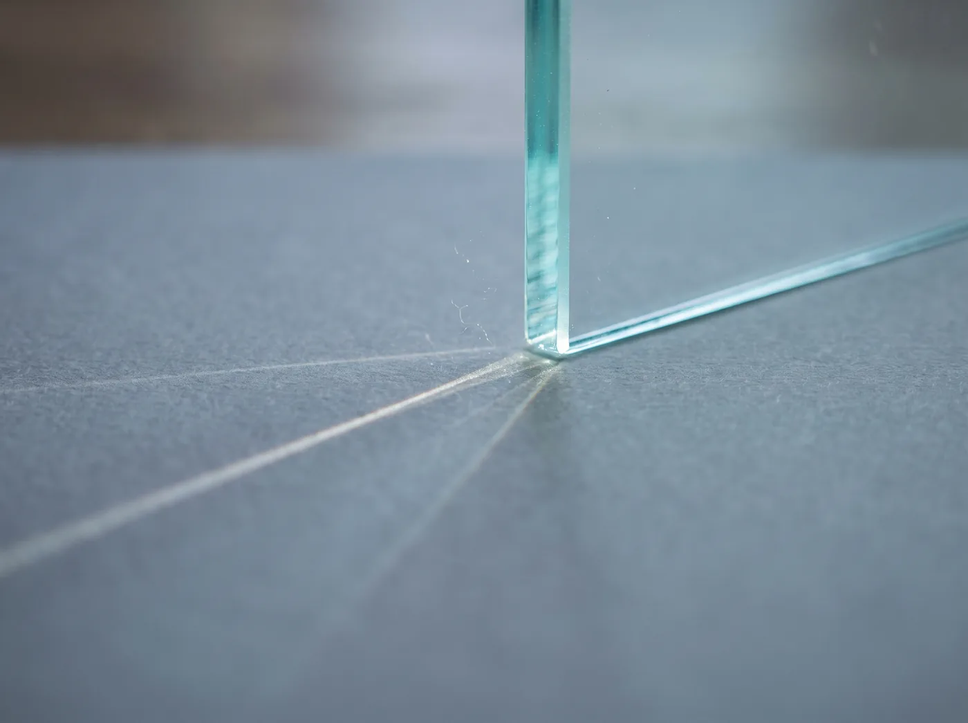 KI-generiert: Licht bricht sich in einer Glasscheibe auf mattem Papier, eine feine Linie zeichnet sich über die Oberfläche, Staub steht im Lichtstrahl.